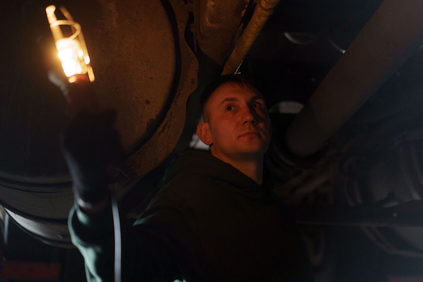 A mechanic holding a lit inspection lamp while working underneath a vehicle in the dark