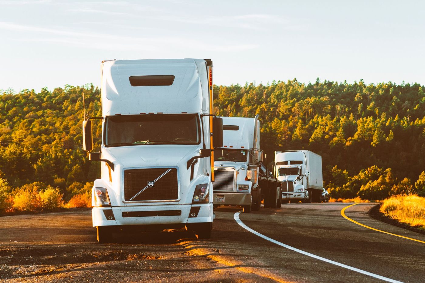 Three tractor-trailers parked on the shoulder of a highway at golden hour