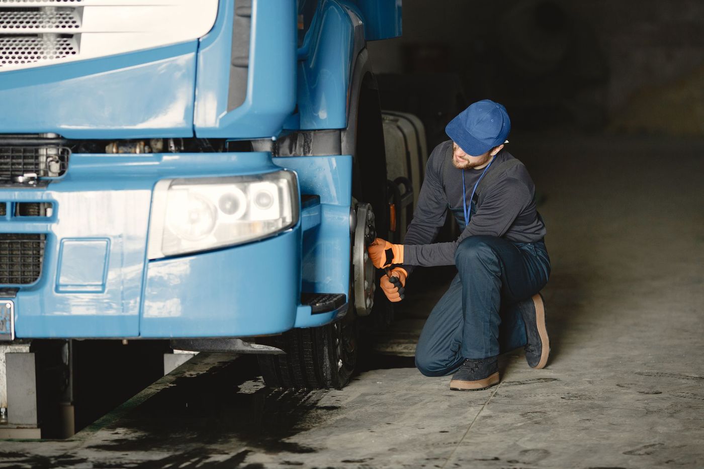 A technician kneeling at the front wheel of a commercial truck with a wrench